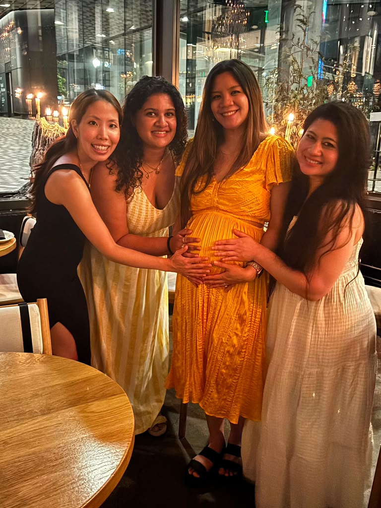 Kat with three friends holding her bump at dinner